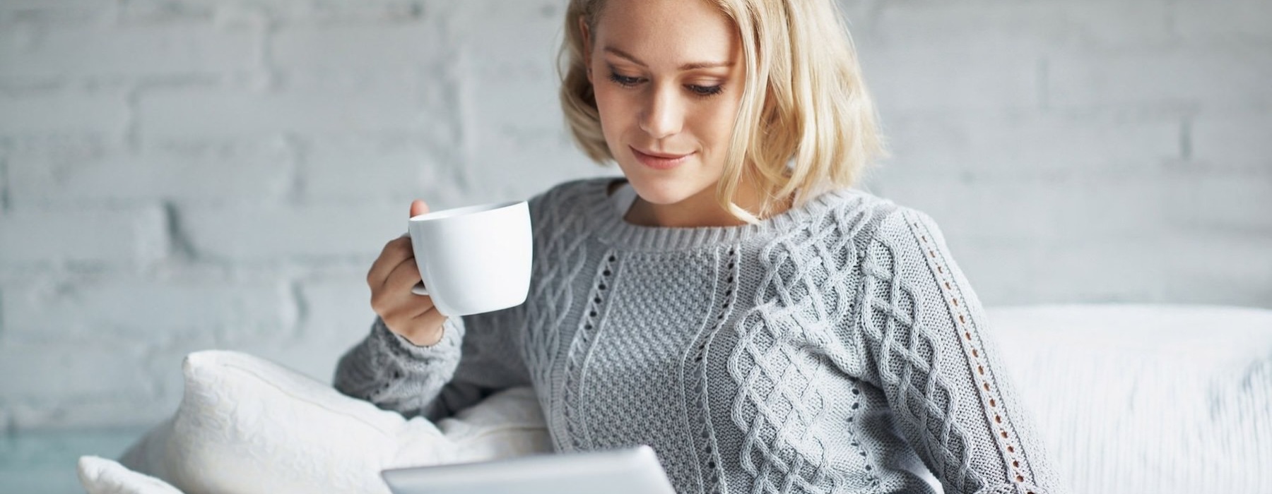 a woman holding a coffee cup looking at a tablet